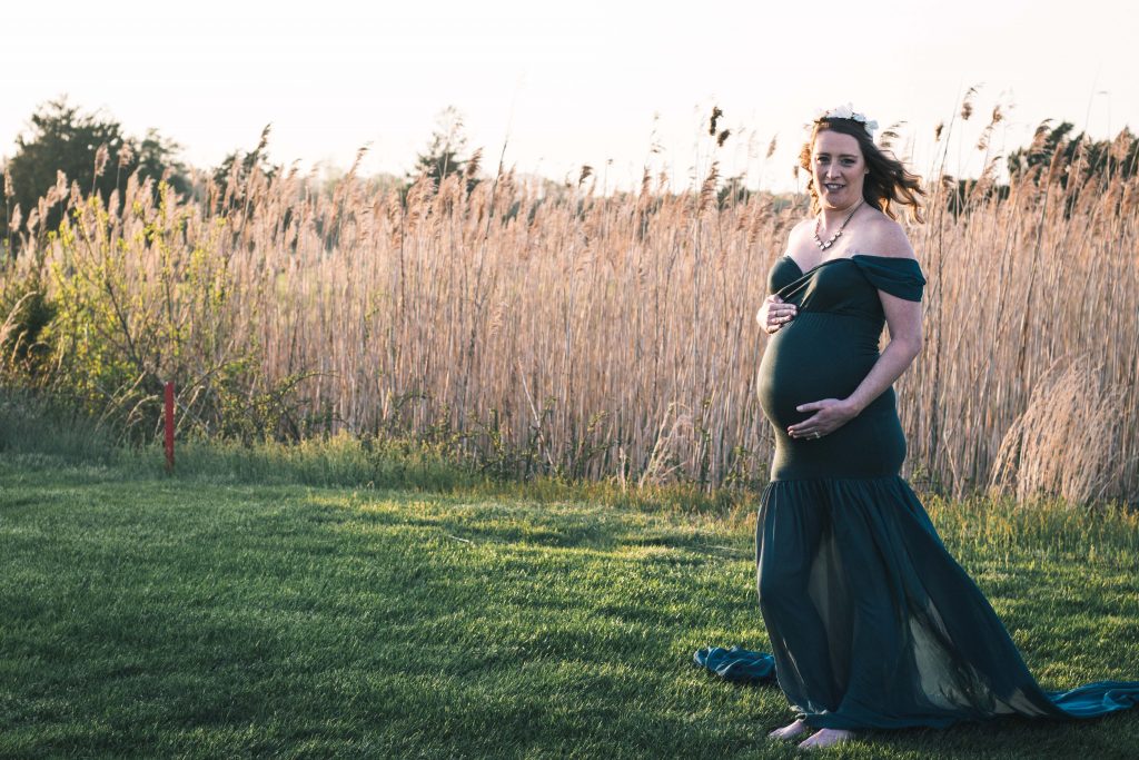A photo of a pregnant woman in front of reeds at sunset 